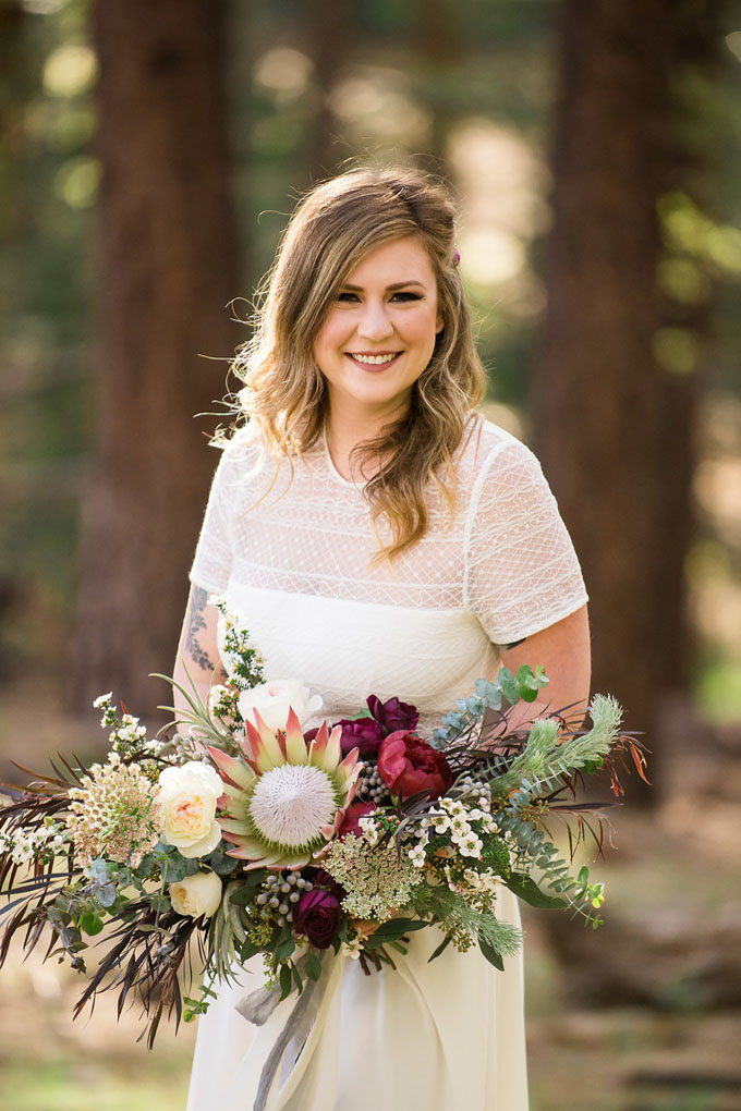 Bride in the forest holds her big bouquet of flowers.