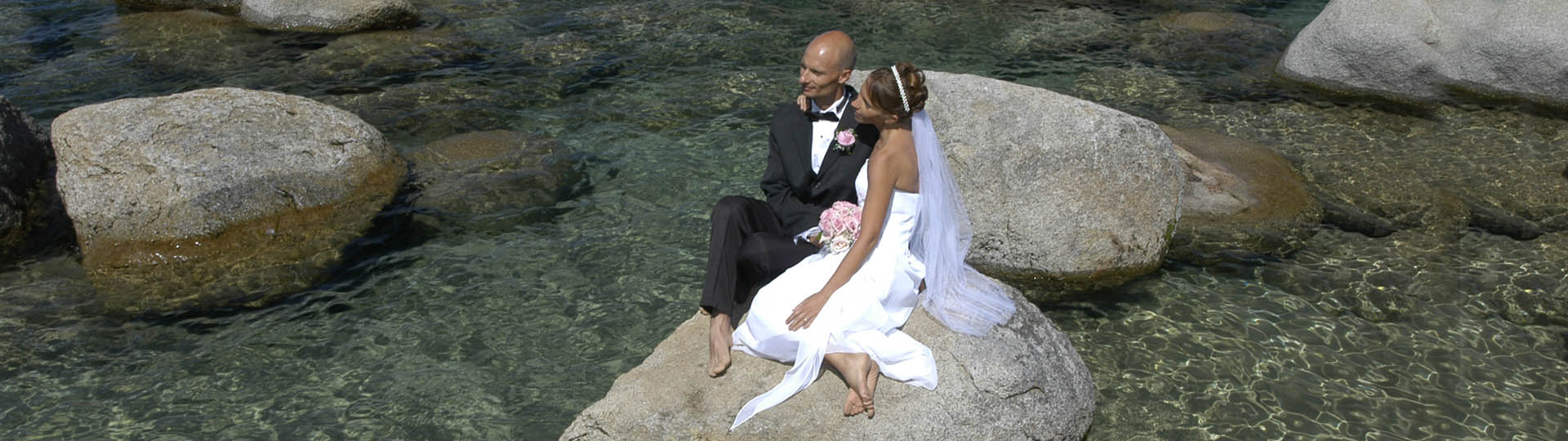 The newly married couple relax on a large rock in the water.