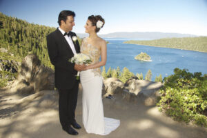 Formally dressed newly married couple are gazing at each other while holding the bride's bouquet and a beautiful Lake Tahoe scene in the background.