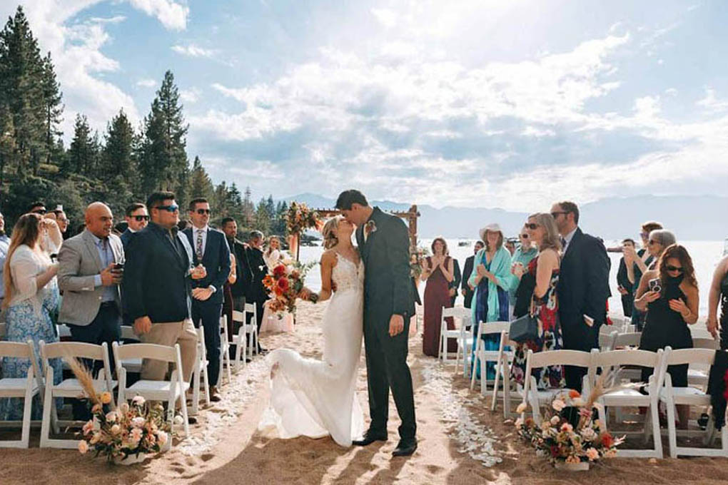 Newlyweds kiss at the end of the sandy beach aisle during the recessional.