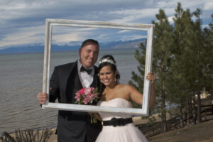 Formally dressed married couple hold up a large picture frame in front of their faces.