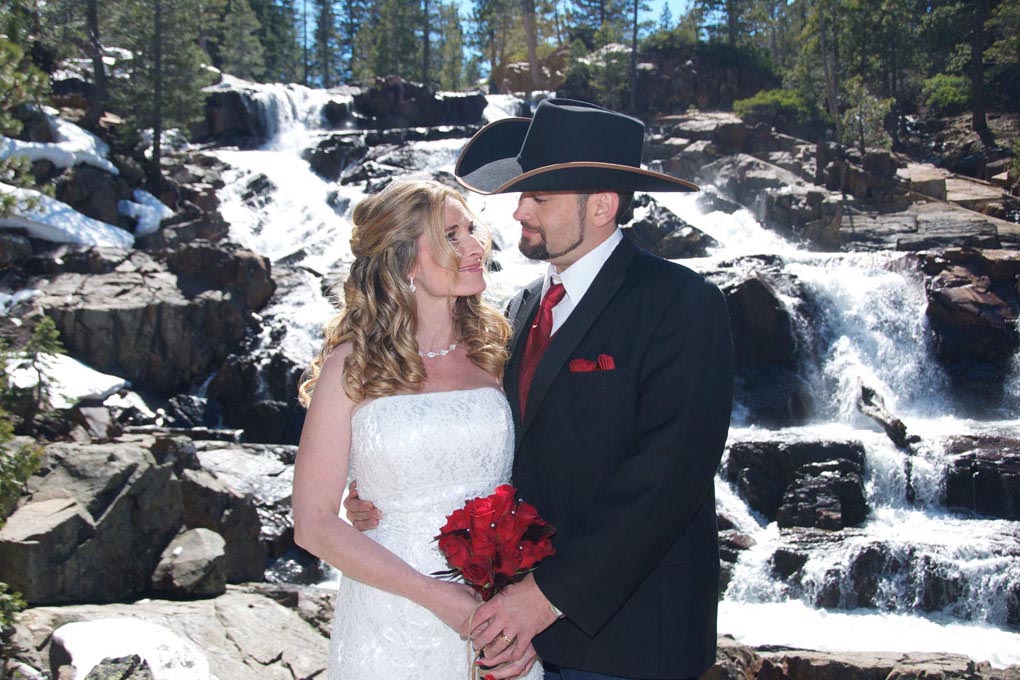 Couple standing together in front of a waterfall.