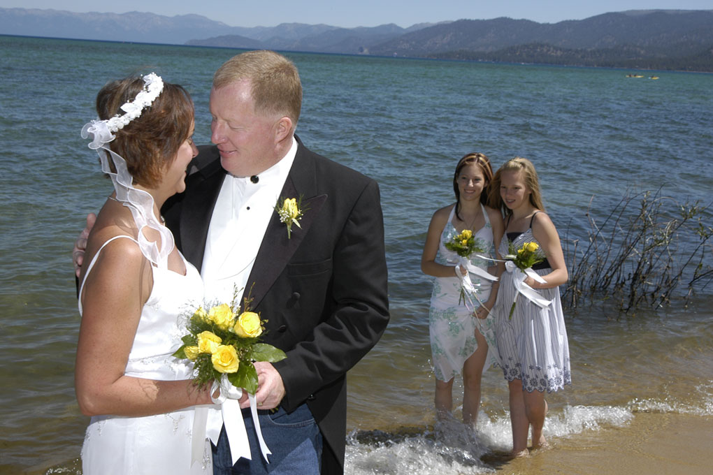 Kids in the water watch the newlyweds embrace each other.