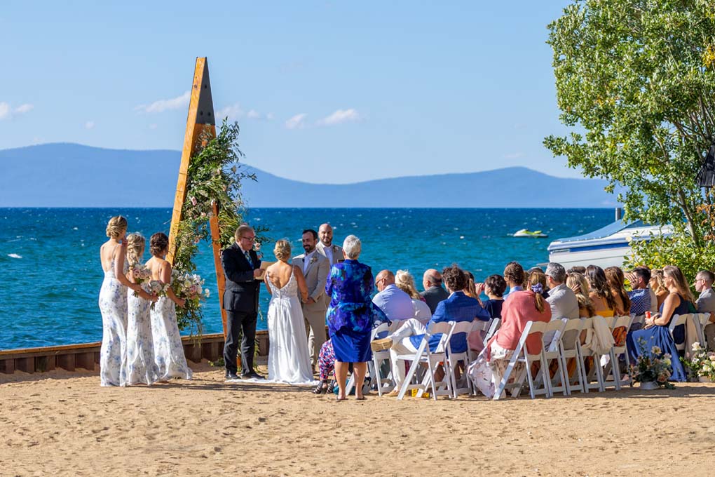 Seated guests watch the bridal party standing in front of the triangular arch during the wedding ceremony.