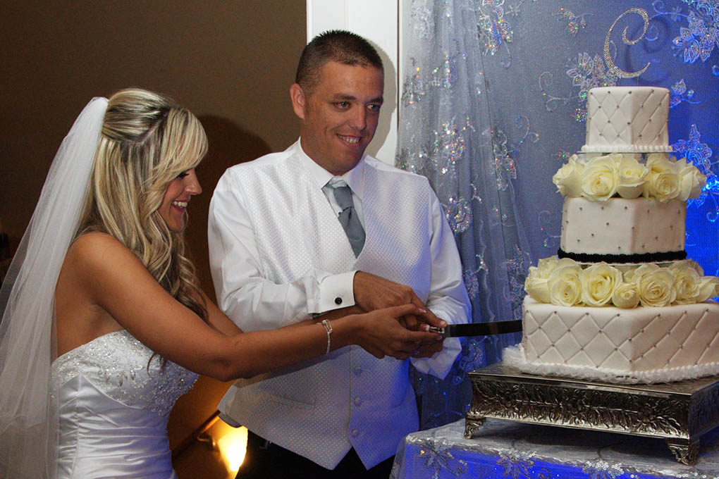 Twosome holding knife together as they slice the first piece of cake,