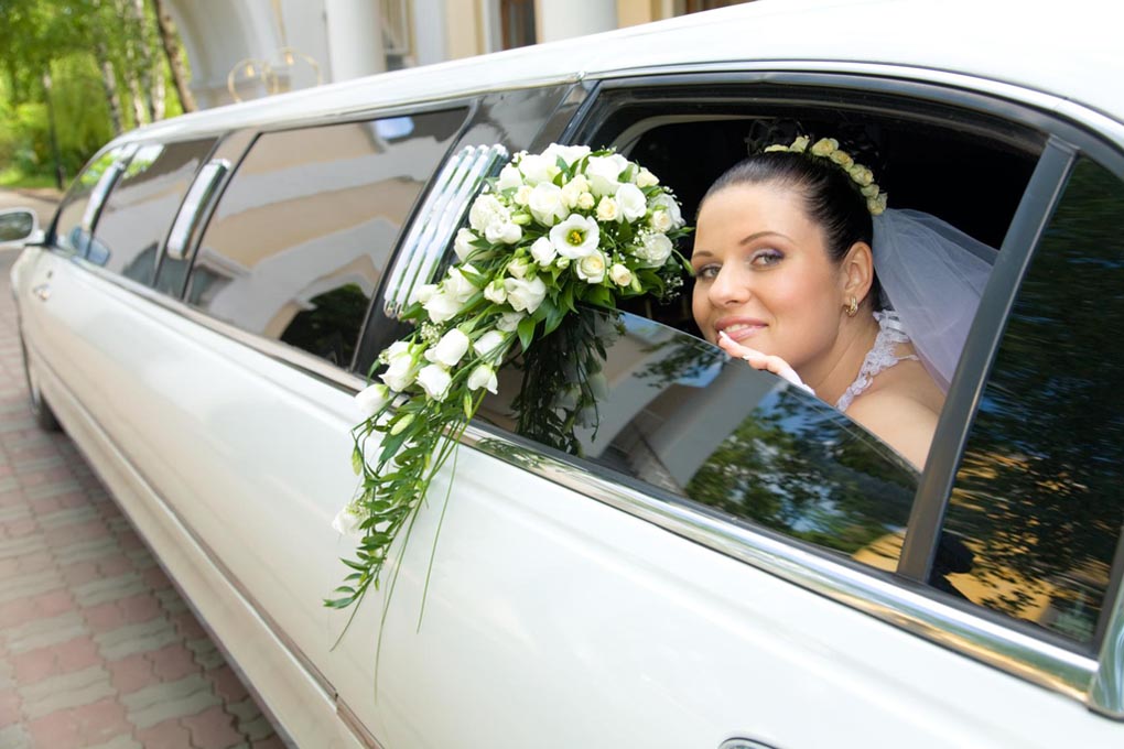 Bride sitting in a limo looking out the window with her bouquet in hand.