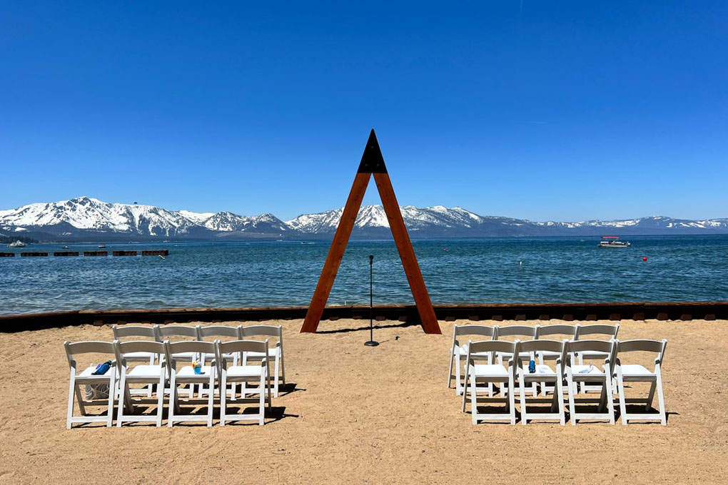 Triangular arch and chairs setup on the beach near the shoreline.