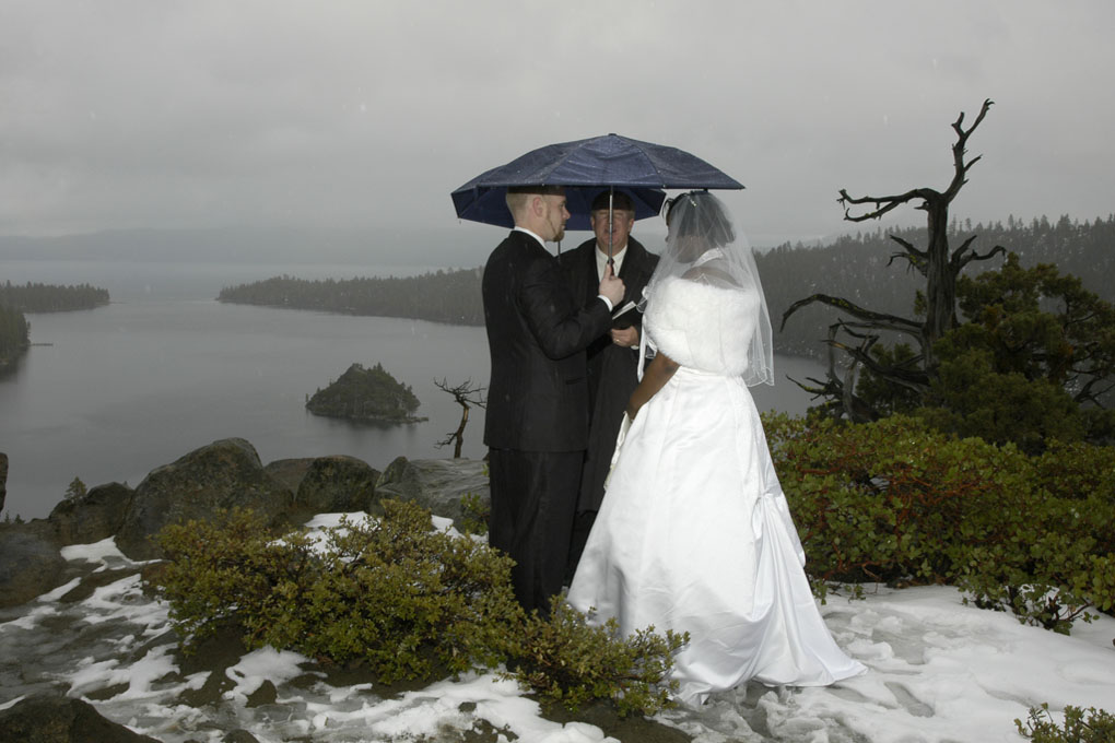 Groom holds an umbrella over the officiant and his bride as the rain falls during their outdoor ceremony.