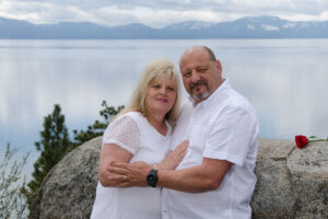 Married pair embrace by a rock and next to a rose.