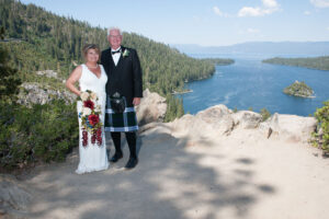 Groom standing next to his bride dressed in a kilt with Emerald Bay and Fannette Island in the background.