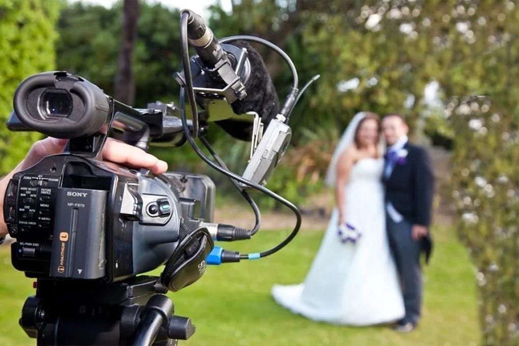 Digital camera is in the foreground and a formally dressed bride and groom are blurred in the background.