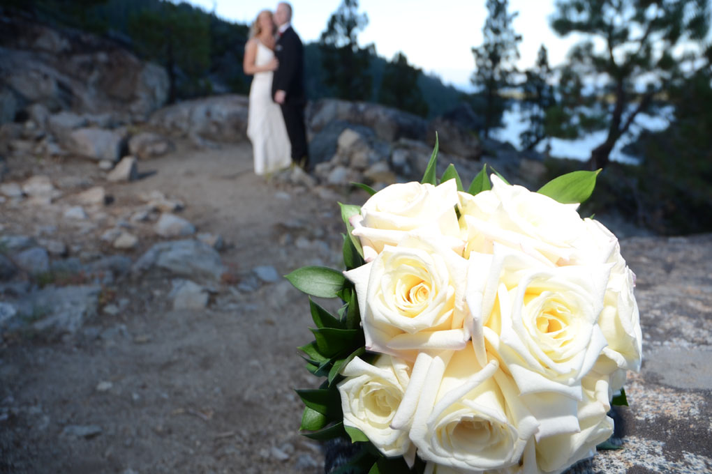 Bouquet of white roses in the foreground with a blurred image of the couple in the background.