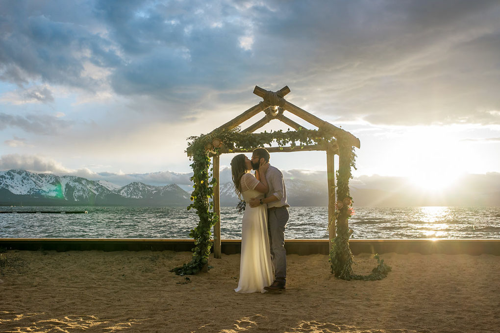 The bride and groom have their first kiss near the arch.