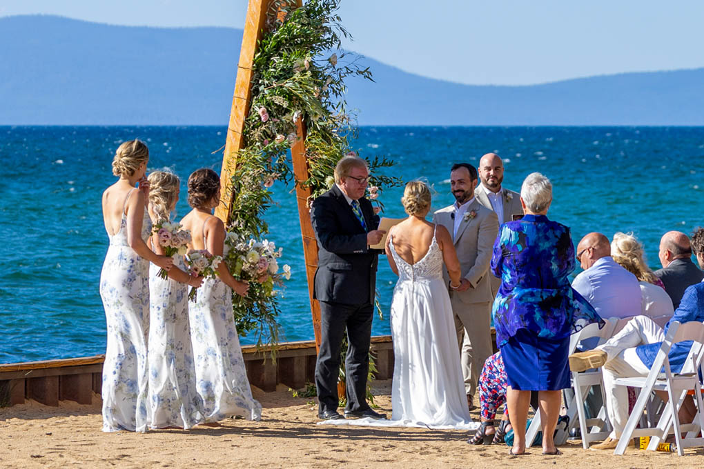 Wedding party and guests watch the service in progress in front of the triangular arch.