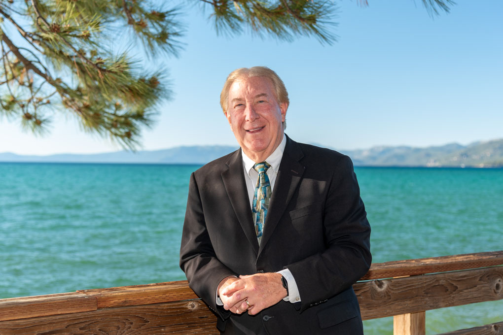 Pastor Robert Orr wearing formal attire leaning casually on a wooden rail.