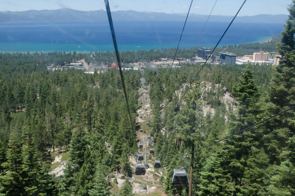Multiple gondola cars ascending the mountainside with an aerial view of Lake Tahoe.