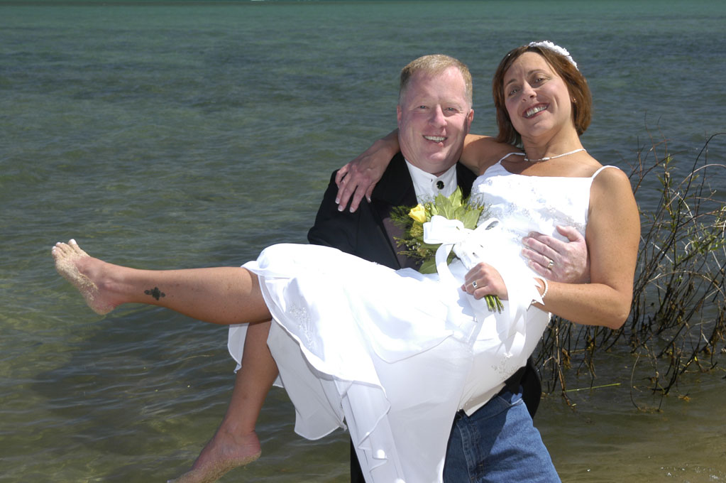 Bride smiles wide as her new husband holds her up in his arms.
