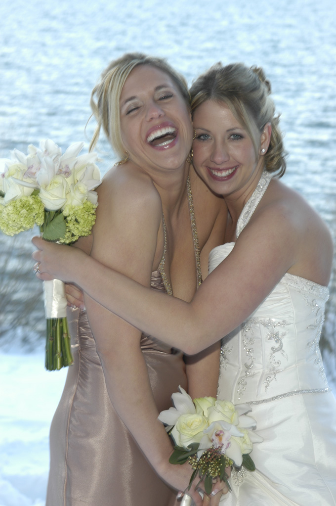 Bride hugging her bridesmaid while she laughs happily.