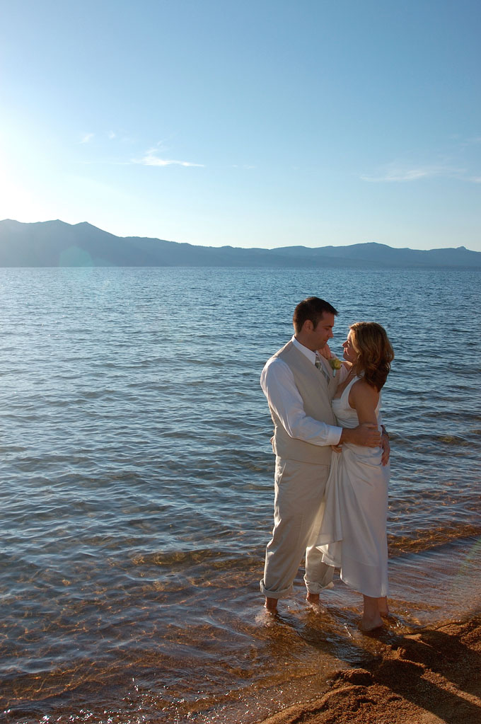 Newlyweds standing barefoot in the lake while dressed in formal attire.