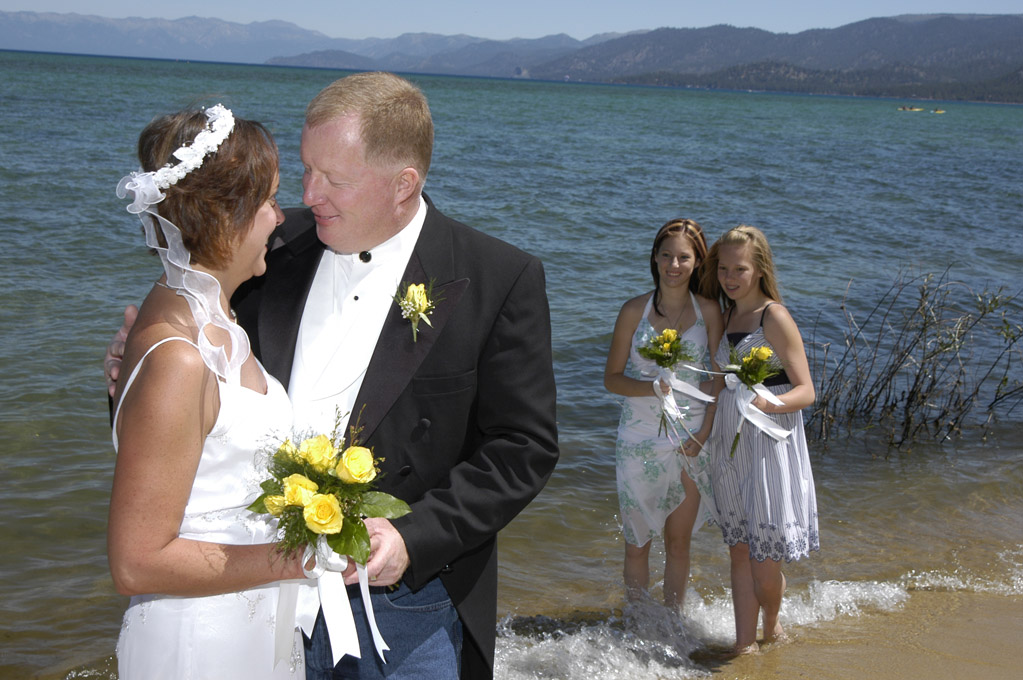 Young daughters of the newly married watch the bride and groom affectionately hug.